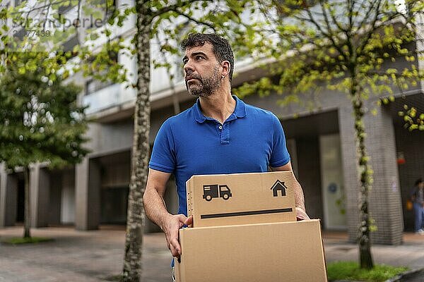 Confident delivery man with package walking on residential street in city