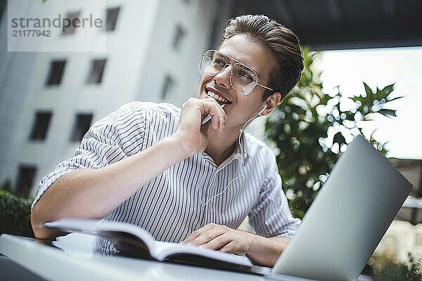 Happy handsome businessman mixes his break and job outdoors  businessman with headphones write some new ideas in notebook sitting in cafe