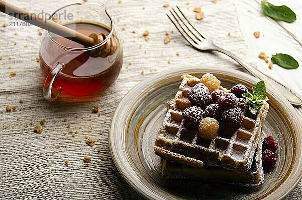 Belgian waffles served with raspberries and mint leaf dusted with powdered sugar on white wooden kitchen table with syrup aside. Selective focus