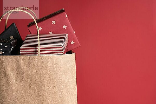 Shopping paper bag full of gifts wrapped in black and red paper  on a red background