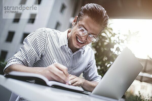 Happy handsome businessman mixes his break and job outdoors  businessman with headphones write some new ideas in notebook sitting in cafe