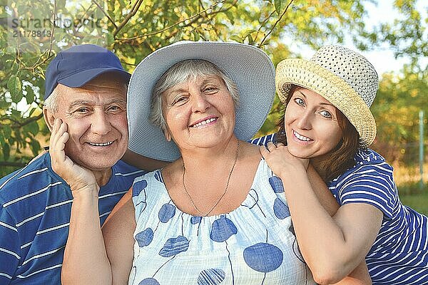 Beautiful senior couple is sitting on the bench in the park with their adult daughter. Grandma and grandpa are hugging and smiling. Real love and family relationship photo. Generations concept