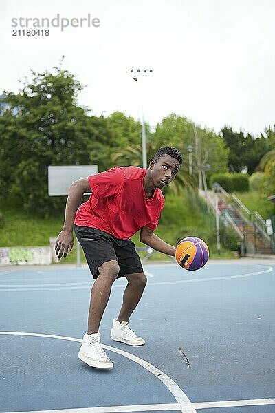 Vertical full length photo of an African american basketball player training in an outdoors facility