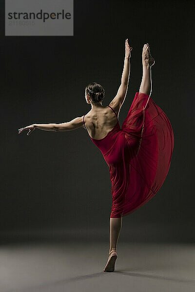 Beautiful girl in red chiffon dress dancing gracefully in dark room rearview