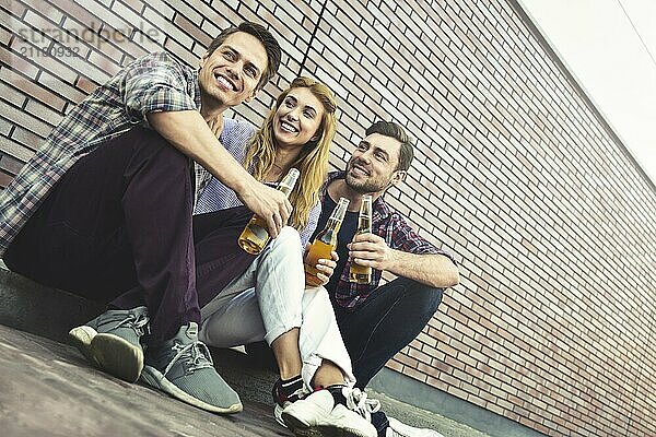 The three happy friends enjoying with beer on a brown brick wall background