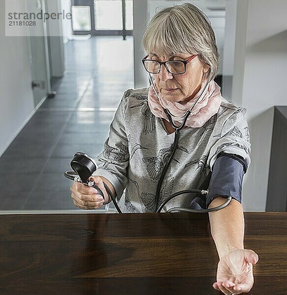 Seniorin prüft Blutdruck einem Tisch mit Messgerät