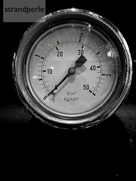 Monochrome image of a round pressure meter with a numbered dial on a dark background