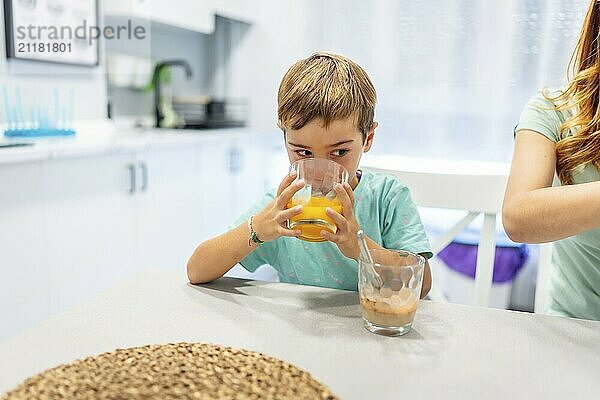 School boy drinking orange juice at home with his mother at the side before going to school