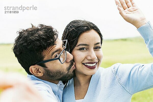 Selfie of young happy couple kissing in the field. Cute couple in love taking a selfie in the field  looking at the camera