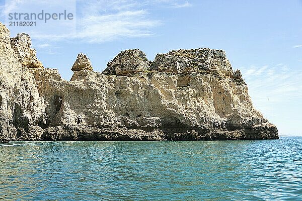 Atemberaubende Felsformationen an der Küste von Lagos in Portugal erheben sich majestätisch aus dem klaren türkisfarbenen Wasser unter einem strahlend blauen Himmel und verkörpern die Schönheit und Ruhe einer unberührten Naturlandschaft