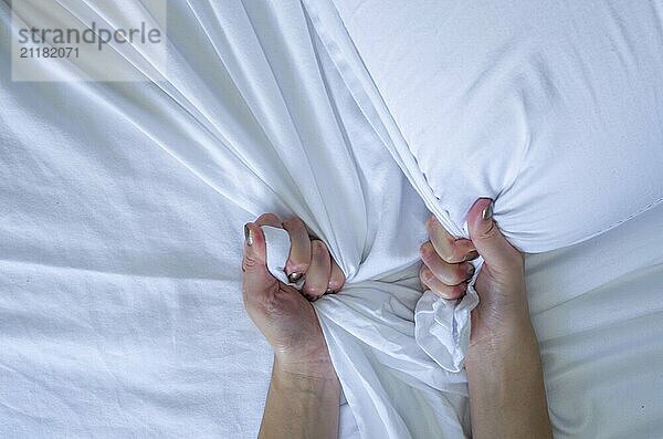 Hand sign orgasm of woman on white bed  Hand of female pulling white sheets in ecstasy  feeling and emotion concept