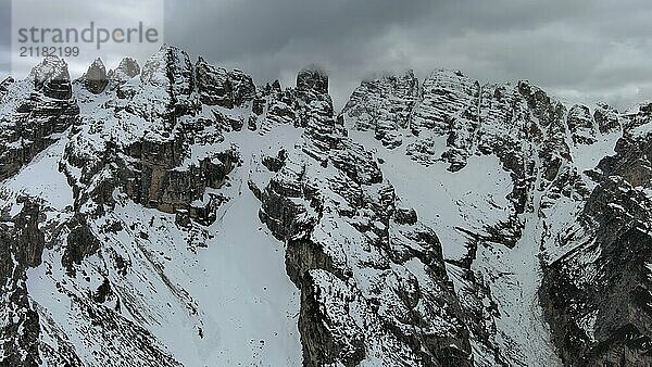 Luftaufnahme von erstaunlichen felsigen Bergen im Schnee unter stimmungsvollen grauen Wolken  Dolomiten  Italien  Europa