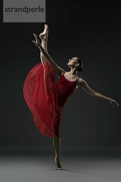 Slim girl wearing red chiffon dress dancing barefoot in the dark room