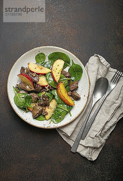 Gesunder Salat mit eisenreichen Zutaten Hühnerleber  Äpfel  frischer Spinat und Walnüsse auf weißem Keramikteller  dunkelbrauner rustikaler Steinhintergrund von oben  Foodfotografie