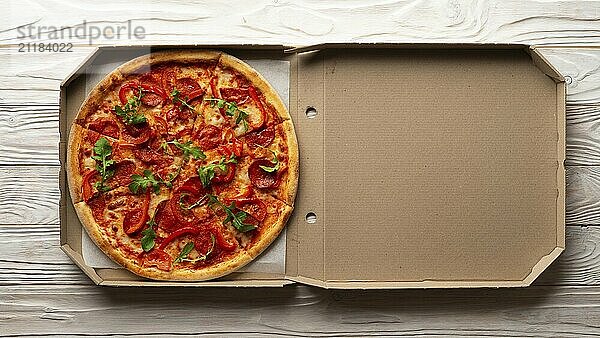 Pepperoni pizza with bell peppers and arugula in open carton box on white wooden kitchen table flat lay view. Copy-space