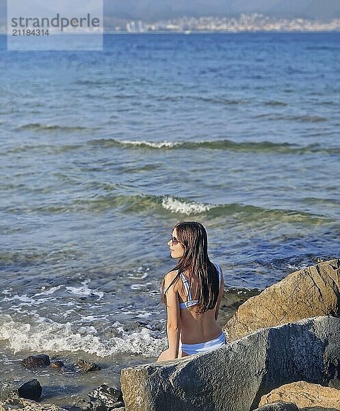 Rückansicht schöne junge Frau im Badeanzug sitzt auf den Felsen am Meer Ufer ein Sonnenbad nehmen. Sommerurlaub Entspannung  Sunny Beach Küste von Bulgarien