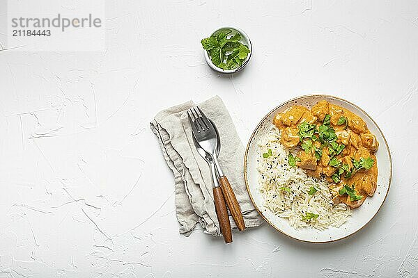 Traditional Indian dish chicken curry with basmati rice and fresh cilantro on rustic white plate on white concrete table background from above. Indian dinner meal  space for text  food photography