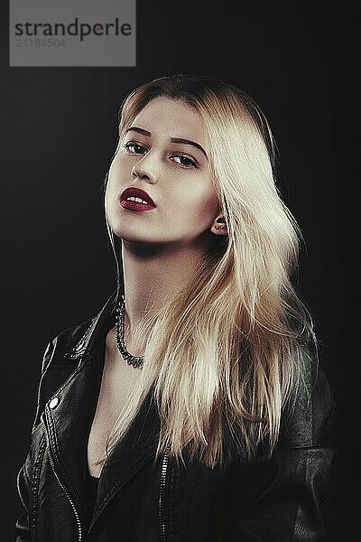 A beautiful  glamour young blond Girl in a black jacket is posing on black background