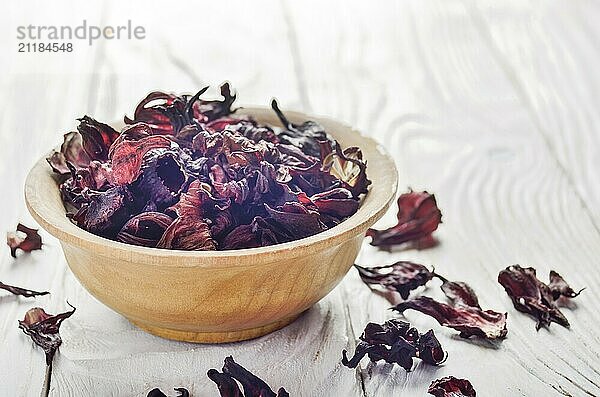 Closeup view at wooden bowl of dry hibiscus petals on white background