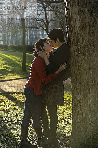 LGBT couple of women sharing a passionate kiss against a tree at sunset