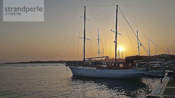 Segelboot in einem Yachthafen bei Sonnenuntergang. Der warme Himmel spiegelt sich auf dem ruhigen Wasser. Die ruhige Schönheit eines Hafens in der Abenddämmerung  die das heitere Ende eines Tages in der Altstadt von Nessebar unterstreicht