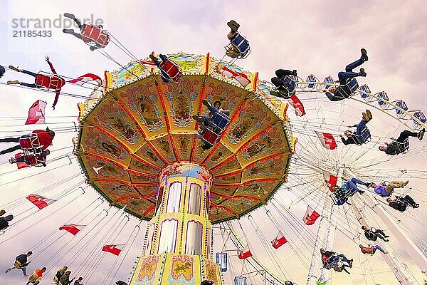 Kettenkarussell in Bewegung mit fröhlichen Menschen vor wolkigem Himmel  Riesenrad  Wellenflug  Cannstadter Volksfest  Stuttgart  Baden-Württemberg