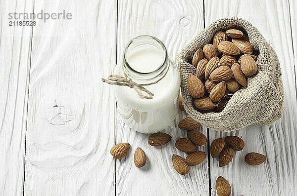 Milk or yogurt in glass bottle on white wooden table with almonds in hemp sack aside