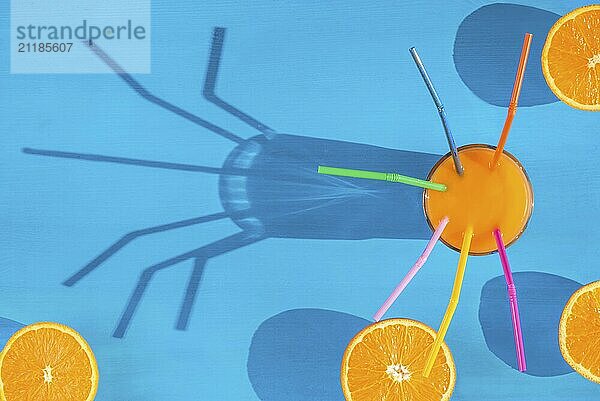 Cheerful image from above with a glass of fresh orange juice with straws in it and orange halves on a blue background  in natural light with shadows