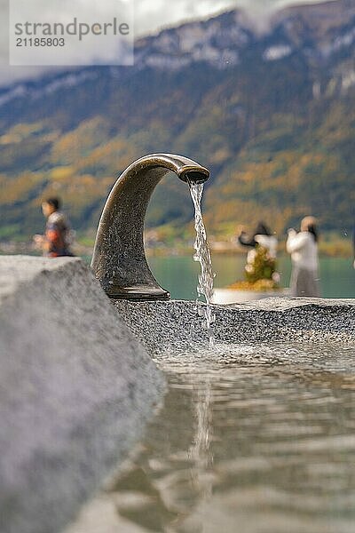 Brunnen mit fließendem Wasser  Menschen am See mit Bergen im Hintergrund  Brienzer See  Schweiz  Europa