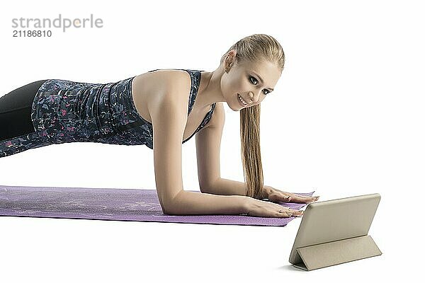 Young pretty woman doing fitness on a mat watching her notebook standing on the floor isolated cropped shot