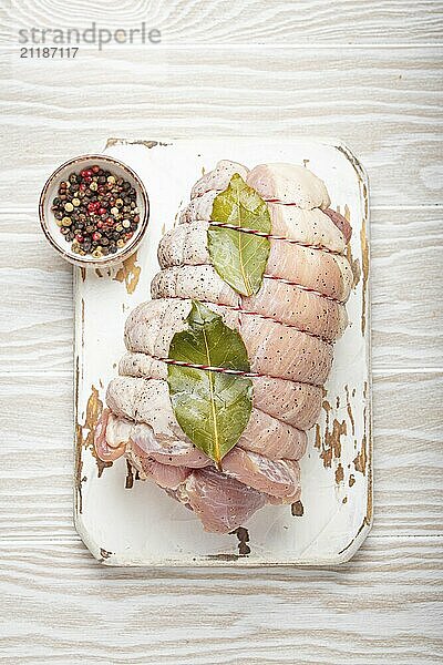 Raw gewickelt gerollt Schweinefleisch in Scheiben geschnitten mit Lorbeerblatt und Gewürze auf weißem Schneidebrett auf rustikalen weißen hölzernen Hintergrund Draufsicht. Schweinerolle bereit zubereitet werden  Lebensmittel Fotografie