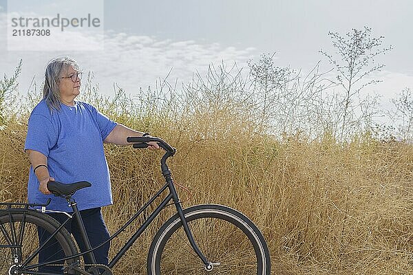 Overweight woman  seen in profile  riding a bicycle on a path covered with vegetation