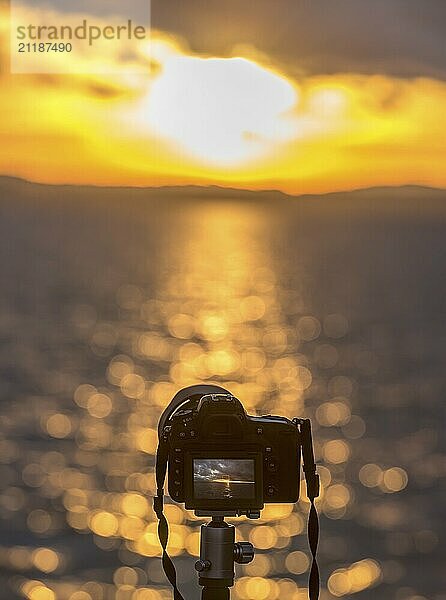 Cropped image with a modern DSLR camera  standing on a tripod  taking a photo with the sunset over the water  in live view mode