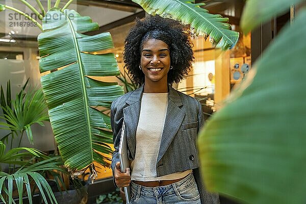 Porträt einer afrikanischen lächelnden Frau vor einem Coworking Space  die einen Laptop hält