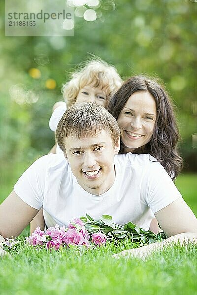 Glückliche Familie im Gras liegend vor frühlingsgrünem Hintergrund