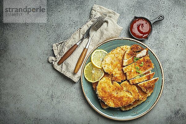 Knusprig paniertes Hähnchenfilet mit grünem Salat und Zitrone auf einem Teller auf grauem Hintergrund mit Ketchup von oben geschnitten. Japanische Art frittierte beschichtete Hähnchenbrust  Platz für Text  Food Fotografie  food photography