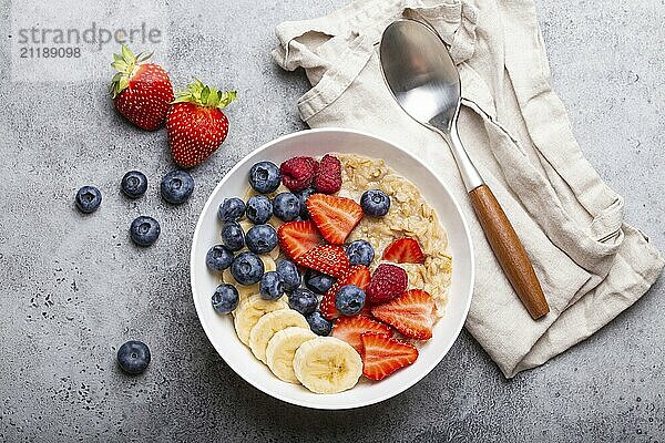 Haferflockenbrei mit Obst und Beeren in Schüssel mit Löffel auf weißem Holz Hintergrund Tisch oben Ansicht  hausgemachte gesundes Frühstück Müsli mit Erdbeere  Banane  Heidelbeere  Himbeere  Lebensmittel Fotografie  food photography