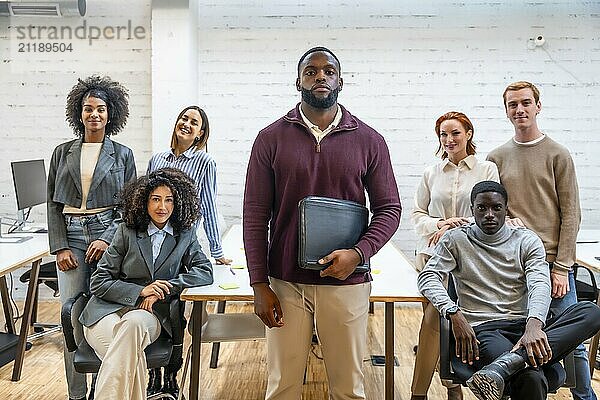 Ernster afrikanischer Mann steht in einem Coworking  umgeben von Kollegen in einem modernen Büro