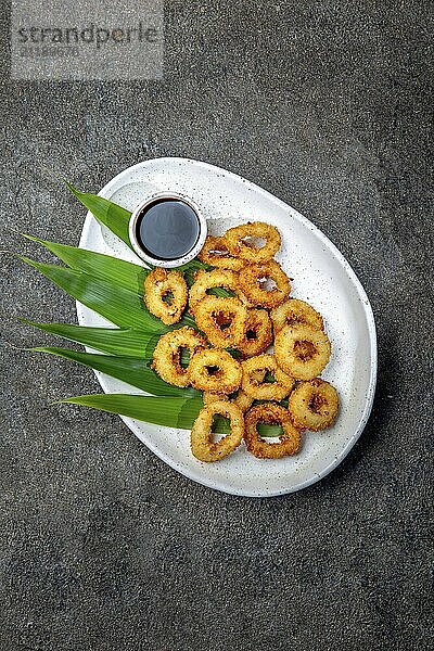 Food  Food  Fried squids rings on white plate decorated with tropical leaves  gray concrete background  top view