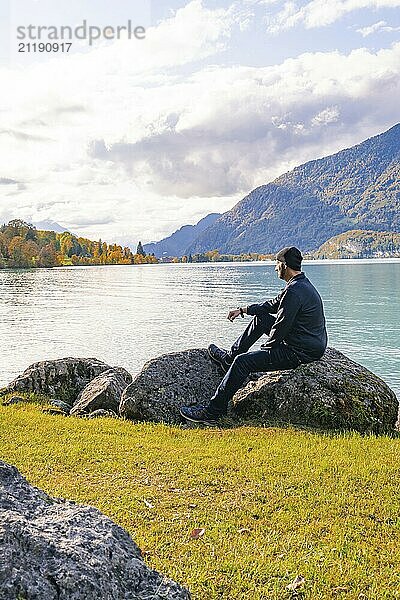 Mann sitzt auf Felsen am Seeufer und genießt die ruhige Berglandschaft  Brienzer See  Schweiz  Europa