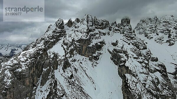 Luftaufnahme von erstaunlichen felsigen Bergen im Schnee unter stimmungsvollen grauen Wolken  Dolomiten  Italien  Europa