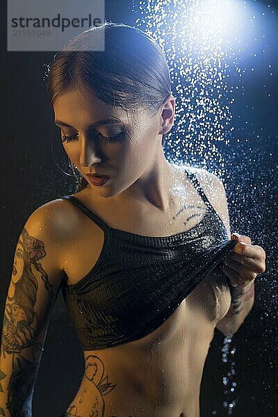 Young tattooed girl wearing sexy shot top having shower in the dark room