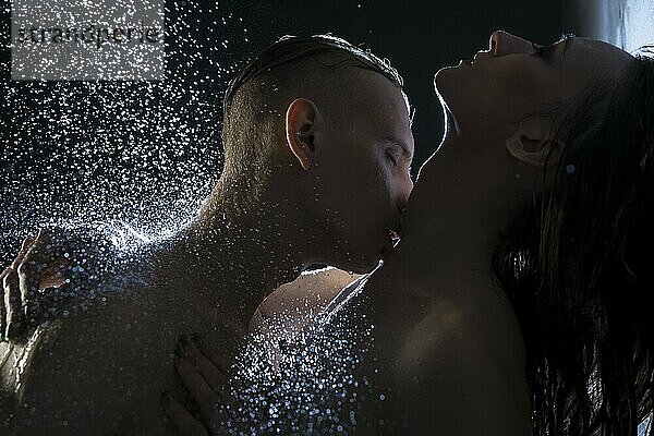 Nude couple embracing in dark shower cropped shot