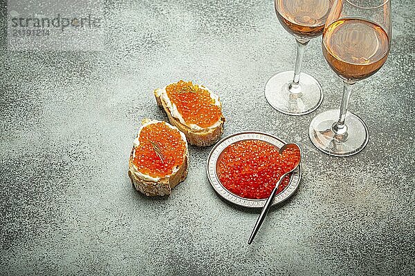 Kleiner Metallteller mit rotem Lachskaviar  zwei Kaviar Toasts Canape  zwei Gläser Champagner von oben auf grauem Betonhintergrund  festliche Luxusdelikatesse und Vorspeise  Foodfotografie