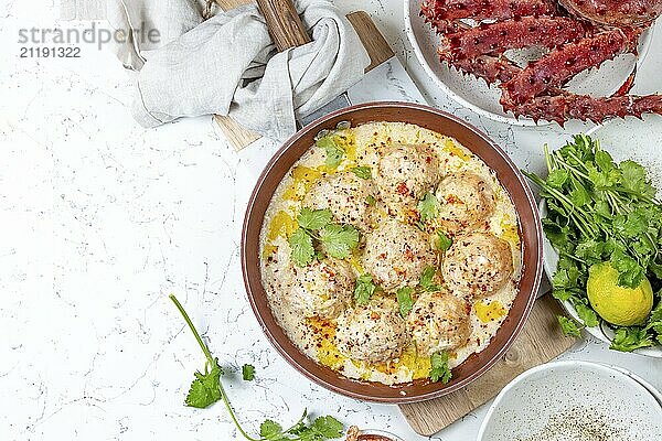 Food  Food  CRABMEATBALLS crab meatballs in white creamy sauce in red pan  whole king crab  cilantro  lemon and white wine on white background