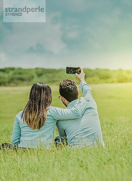 Young happy couple taking a selfie sitting in the field. Couple in love taking a selfie sitting in a beautiful field