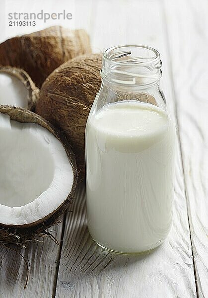 Glass bottle with milk or yogurt on white wooden kitchen table with coconut aside