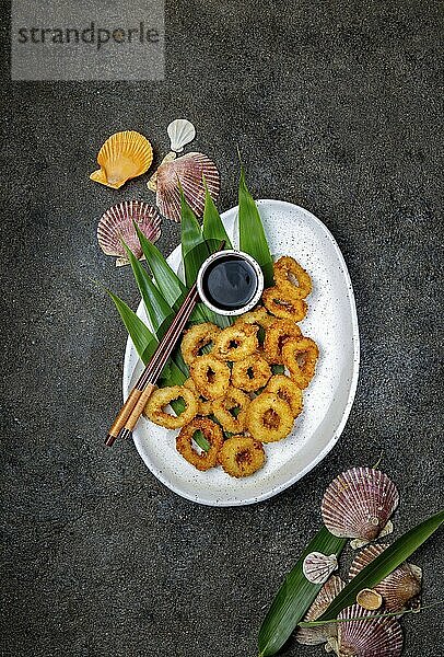 Food  Fried squids rings on white plate decorated with tropical leaves  gray concrete background  top view