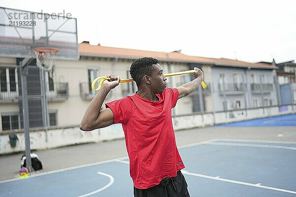 Athletischer afrikanischer Junge dehnt sich mit einem Gummiband in einem städtischen Basketballplatz im Freien