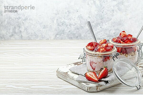 Parfait mit frischen Erdbeeren  Joghurt und knusprigem Müsli in transparenten Einmachgläsern auf weißem  rustikalem Holzhintergrund Schrägansicht  gesundes Frühstück oder leichtes Sommerdessert  Copy Space  Foodfotografie